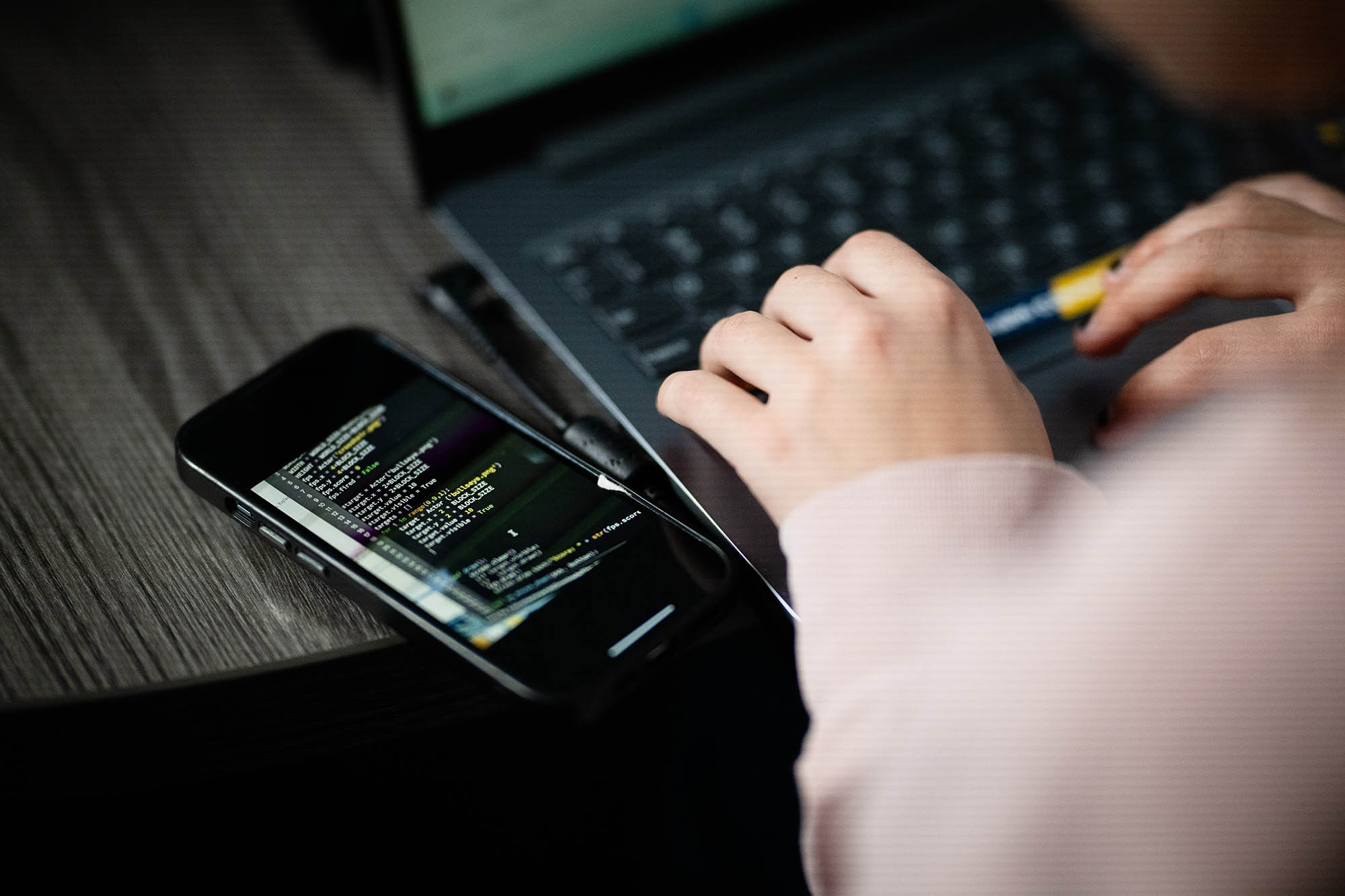 Close-up of a computer science student coding on a laptop and smartphone during a programming session.