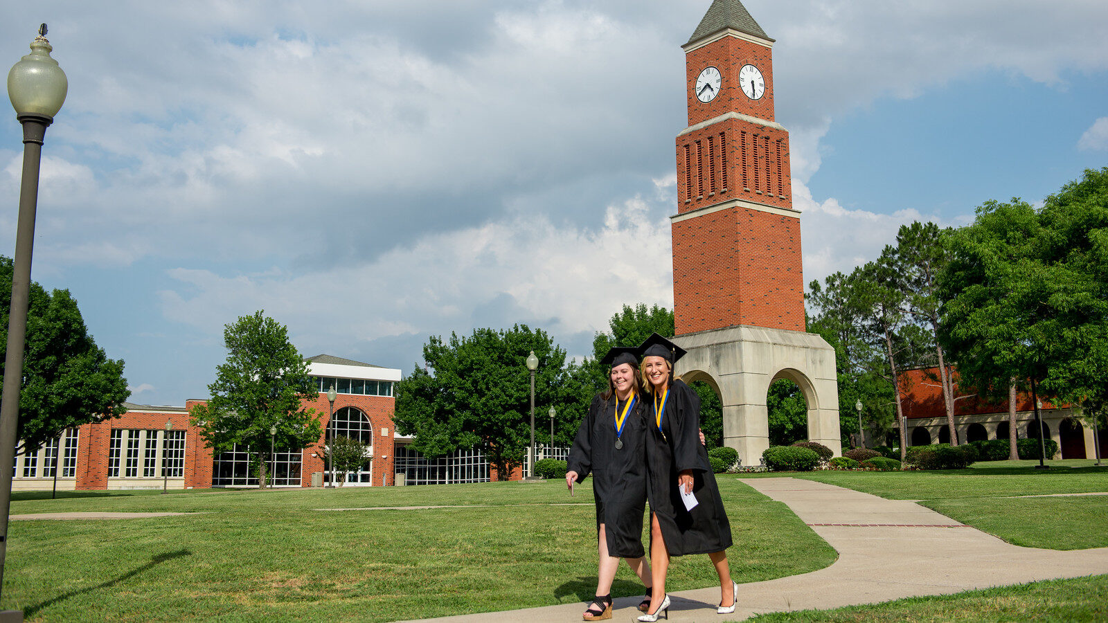 Two graduates walking on the Navarro College campus, smiling after graduation.