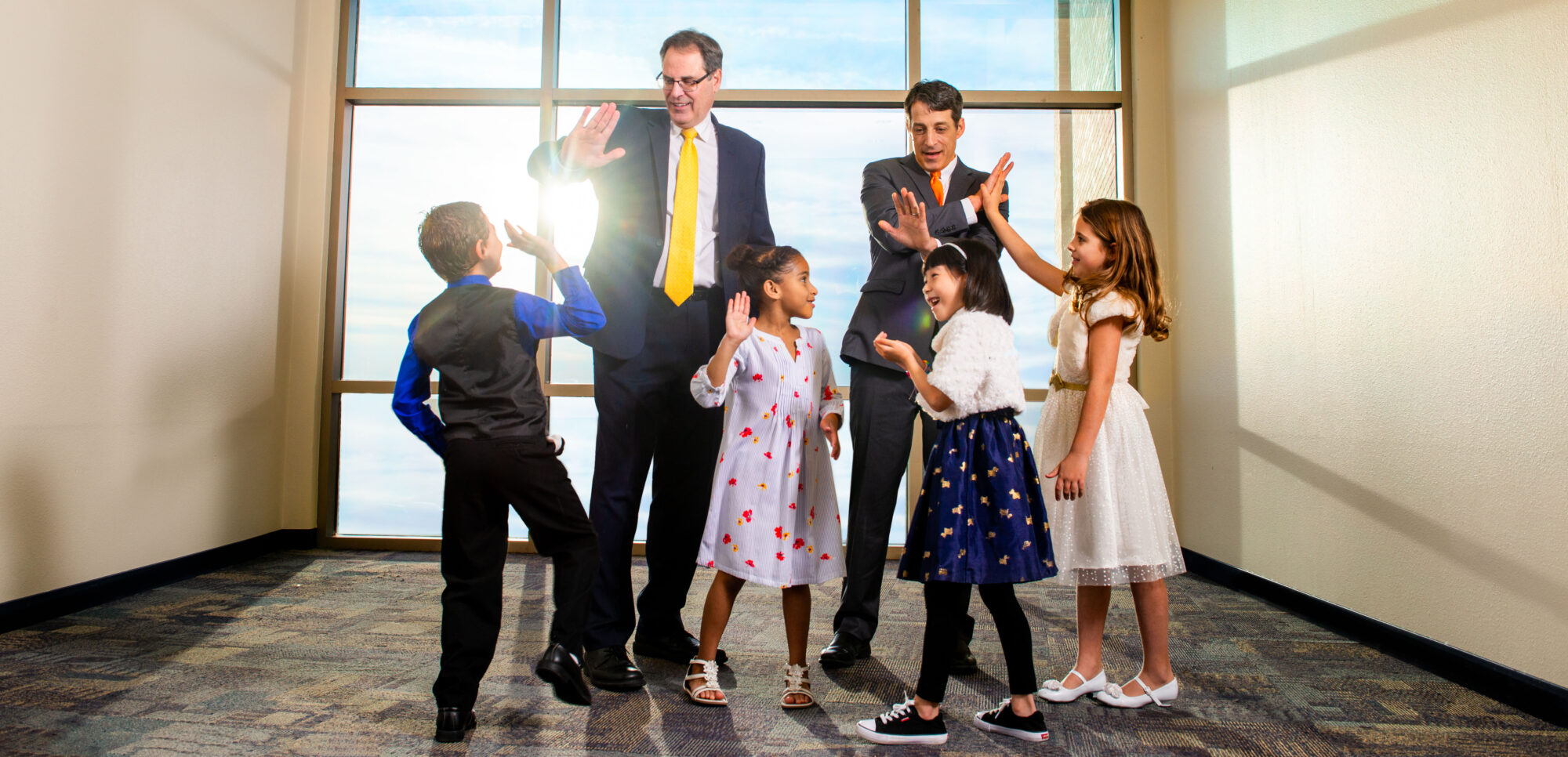 Two men giving four kids high fives.