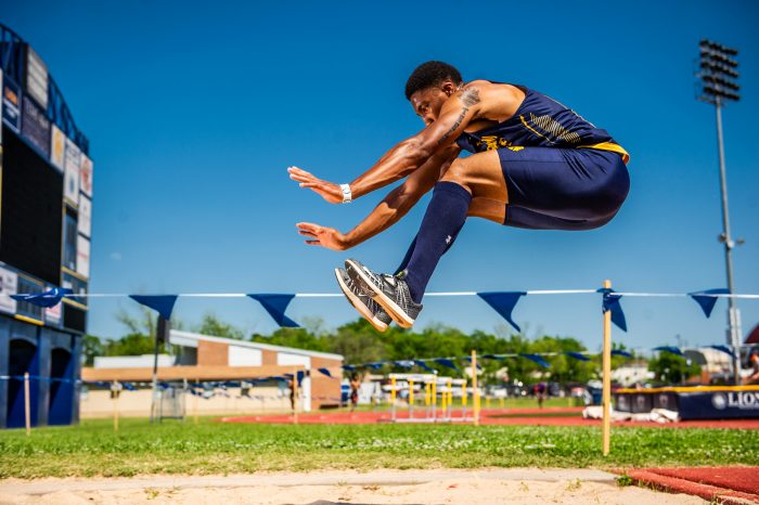 A track and field athlete is depicted in mid-air over a long-jump sand pit.