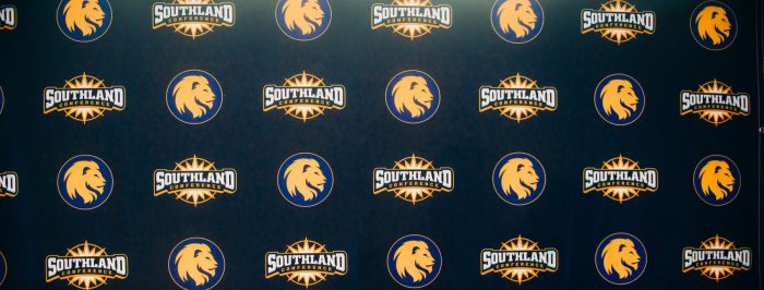 A decorative backdrop featuring the logos of A&M-Commerce and the Southland Conference