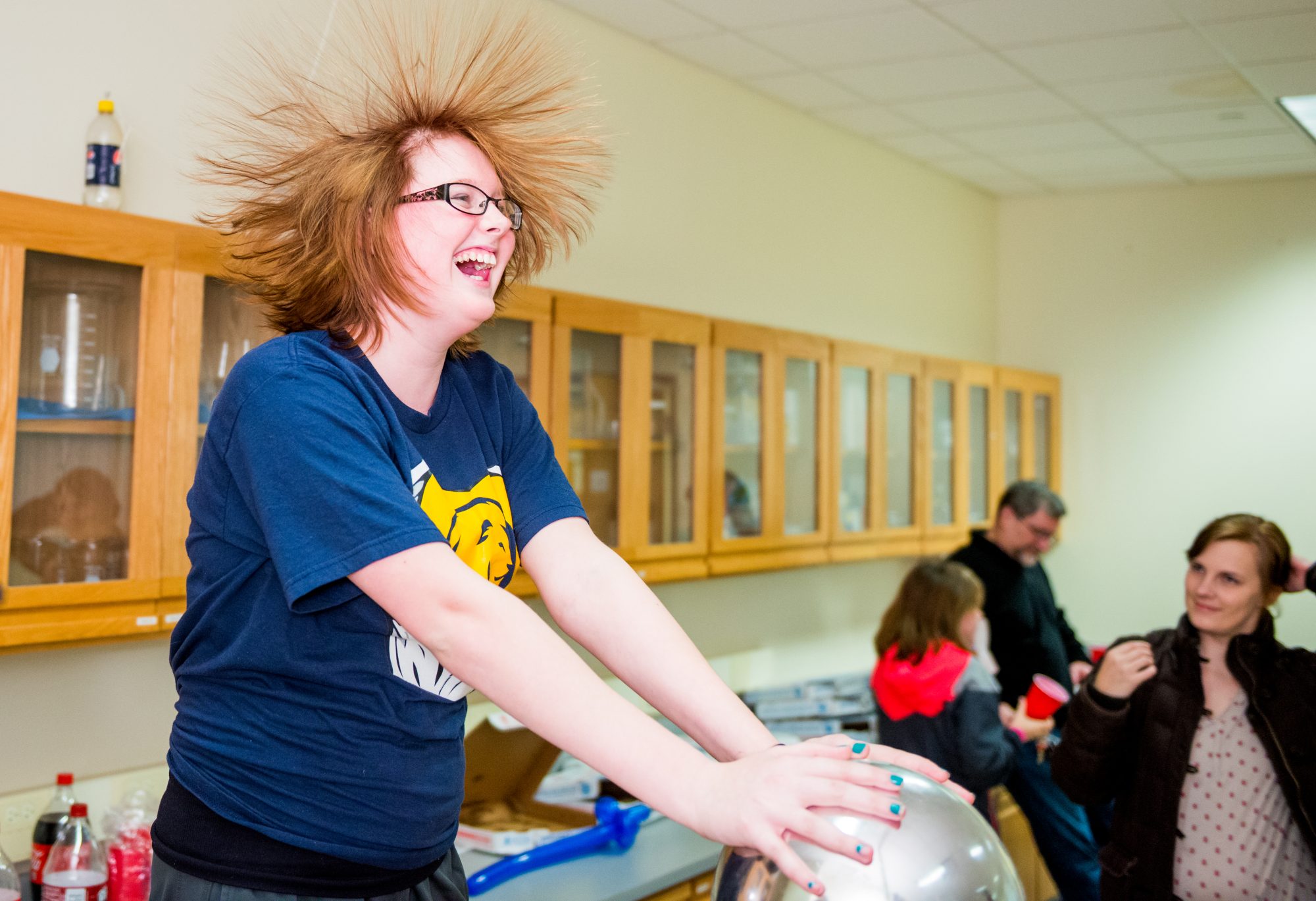 A woman in a physics classroom demonstrates the effects of the Van de Graaff generator.