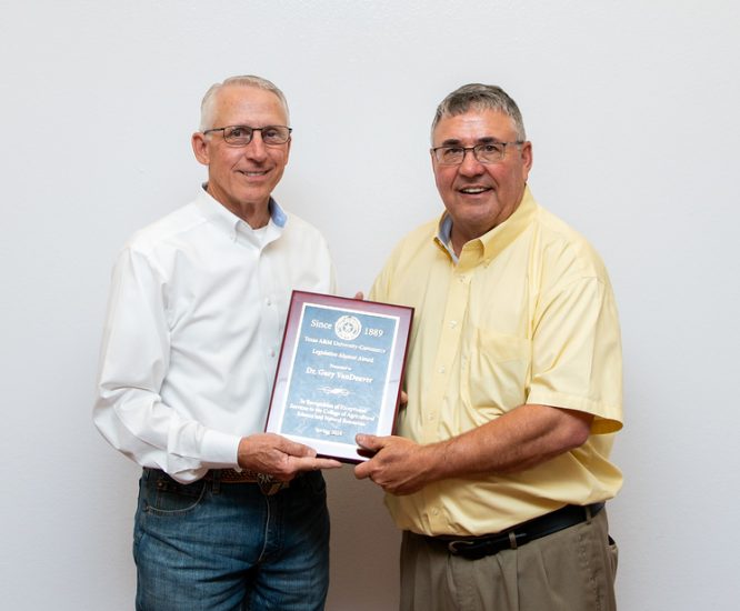 Award recipient and Dr. Harp face the camera with a white backdrop behind them. They both have one hand on a framed award.