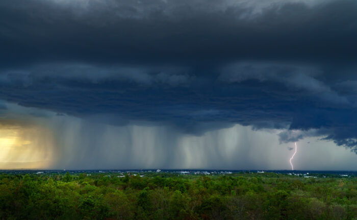 Landscape shows storm clouds overhead with rain coming down in sheets on green landscape.