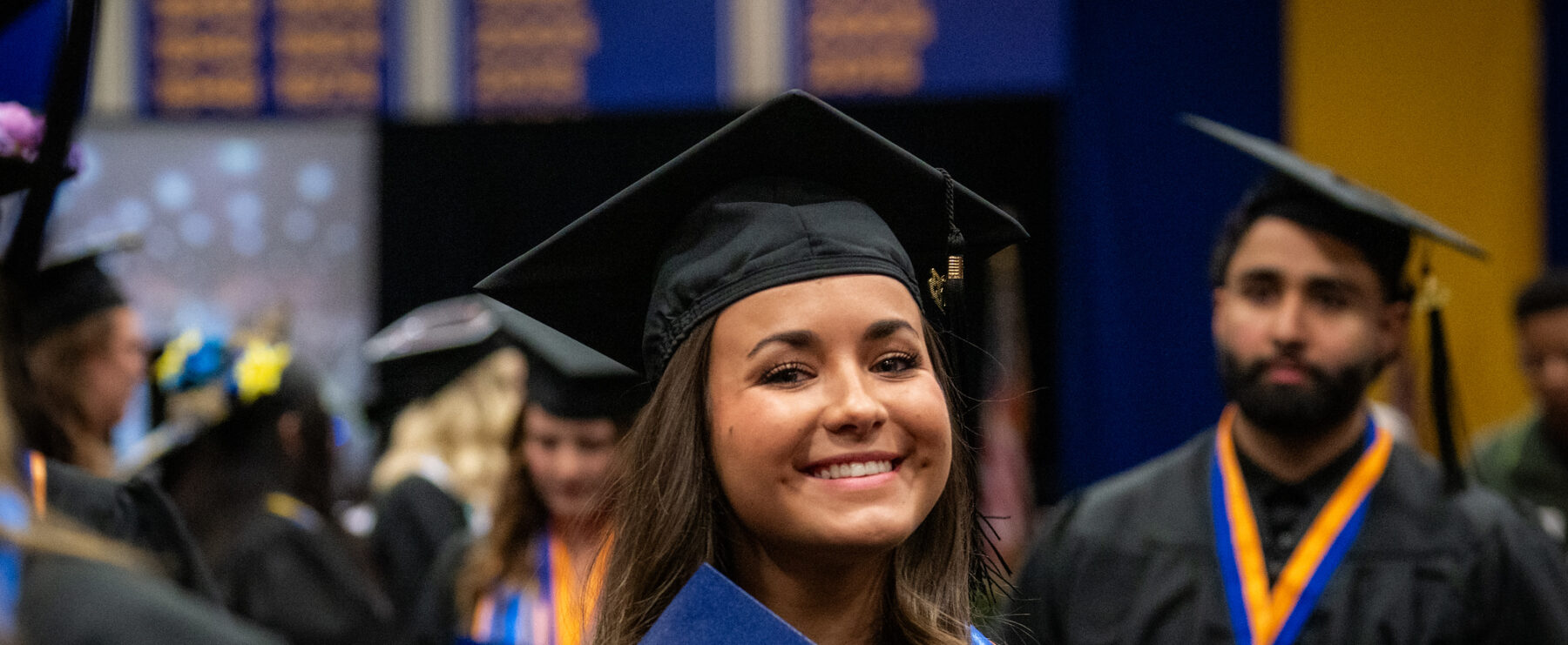 Graduate holds diploma in both hands and smiles at the camera, wearing graduation cap and gown.