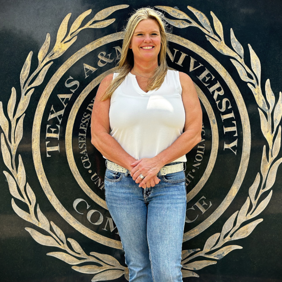 A person standing in front of a large sign bearing the seal of Texas A&M University-Commerce.