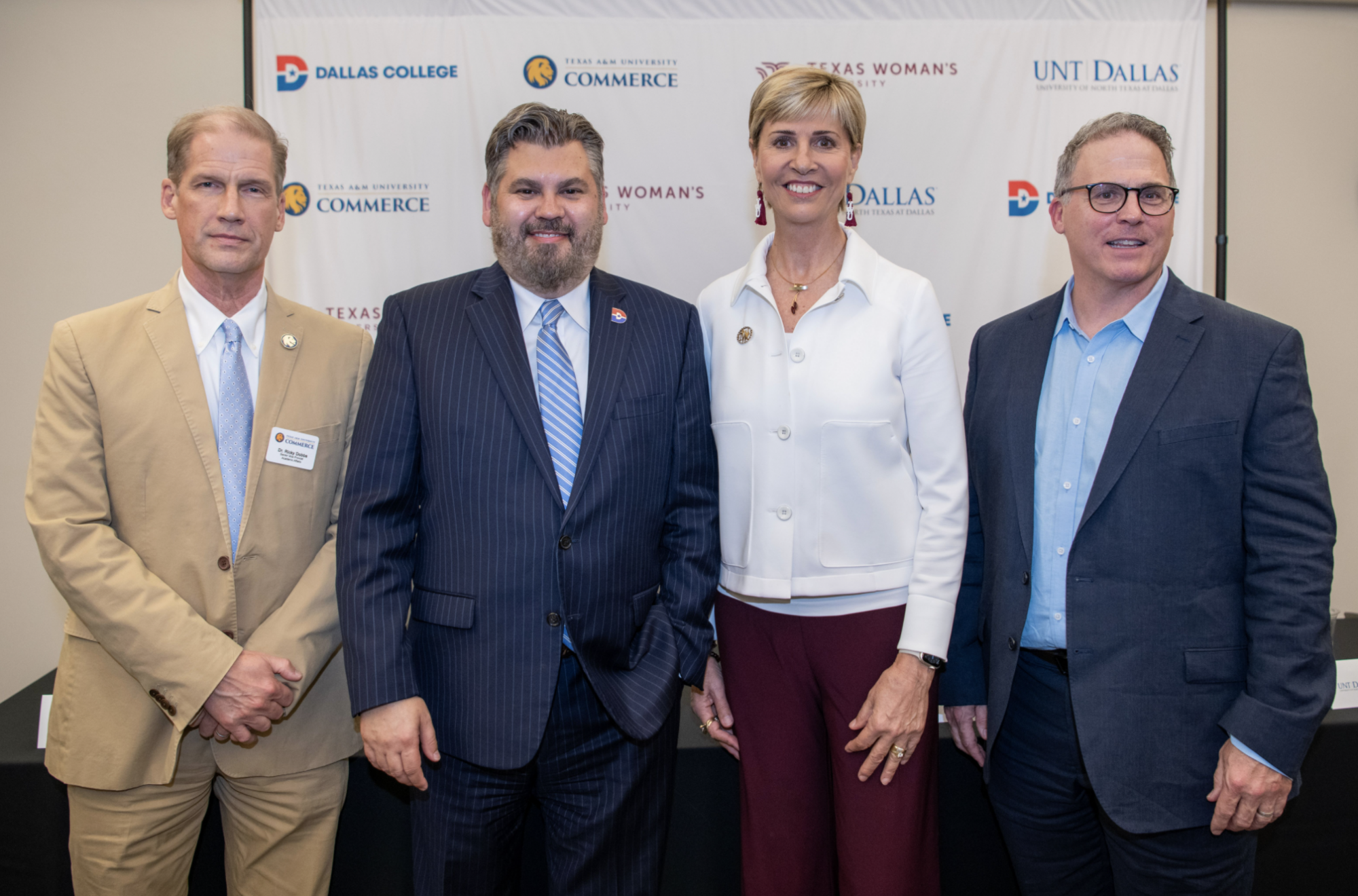 Four administrators of higher education line up for a photo with white backdrop containing the logos of each representative's school.