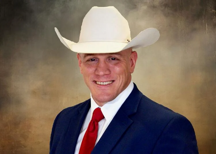 A&M-Commerce alum Joshua Ray poses for a headshot wearing a white cowboy hat and dark business suit with red tie.