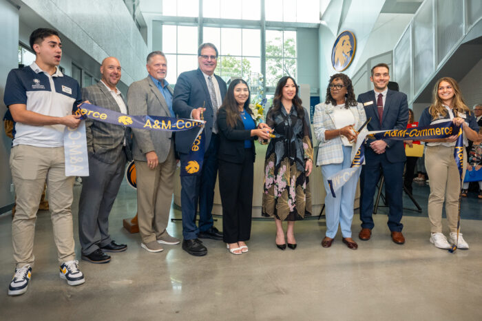 Eight people line up and hold a blue ribbon in front of them, which was cut in the middle.