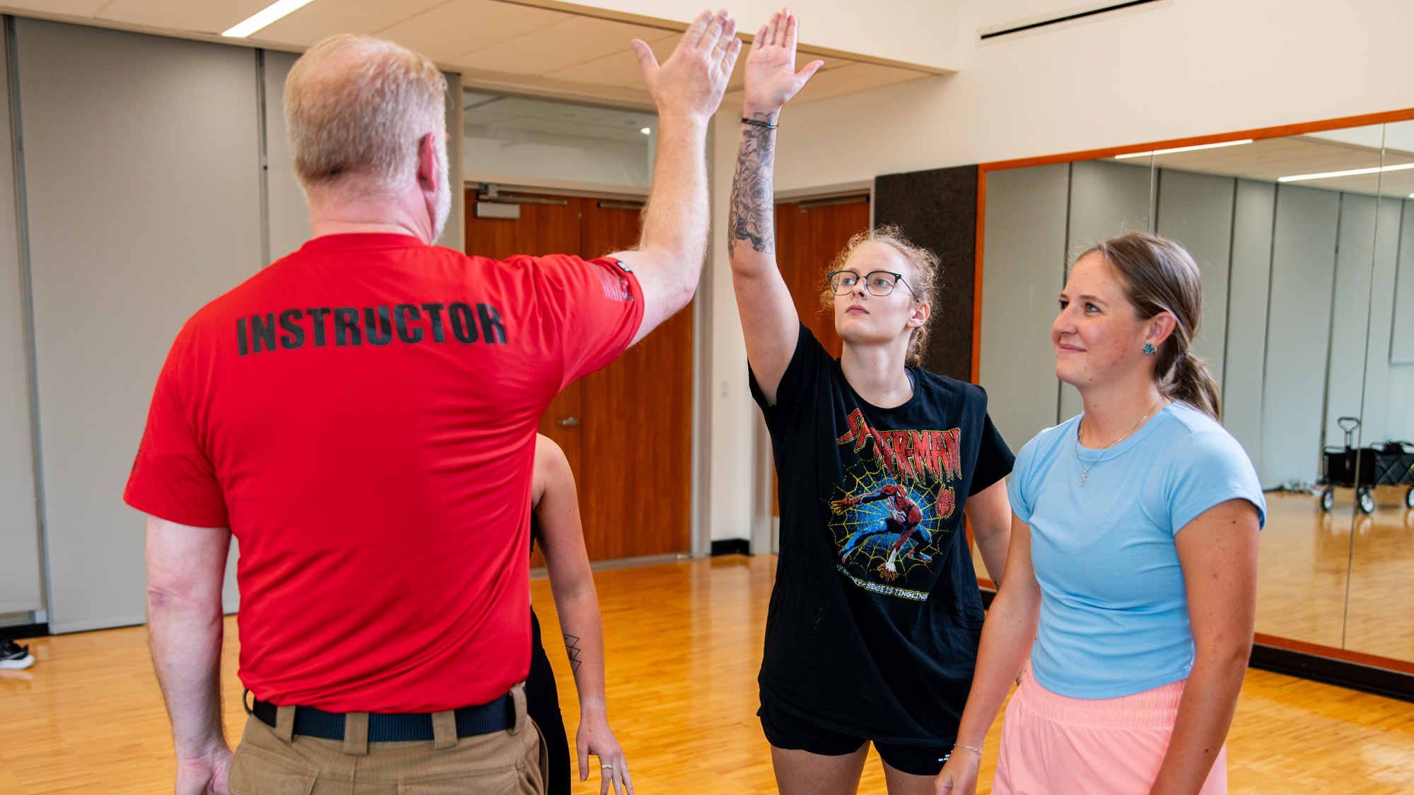 An instructor offers up a high-five and one of three students reaches up to accept the encouragement.