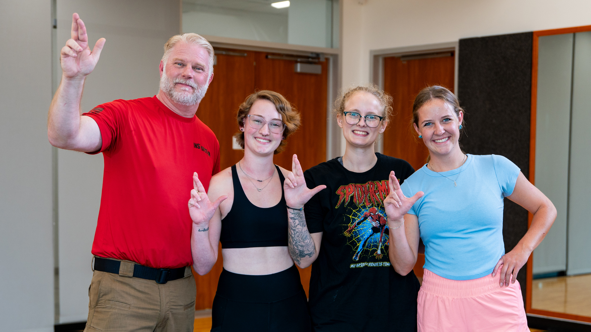 An instructor and three students face the viewer, smiling and holding up their right hands in the "Lucky Lion" hand sign.