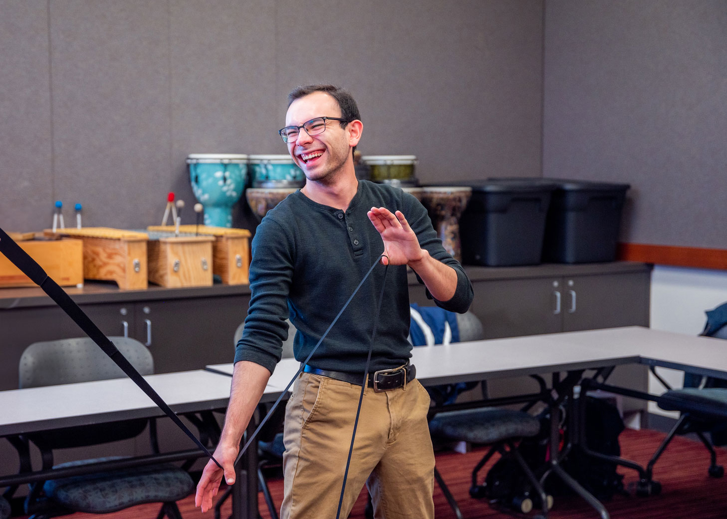 A young man in a casual setting excitingly engages in a musical activity, holding a mallet and smiling widely.