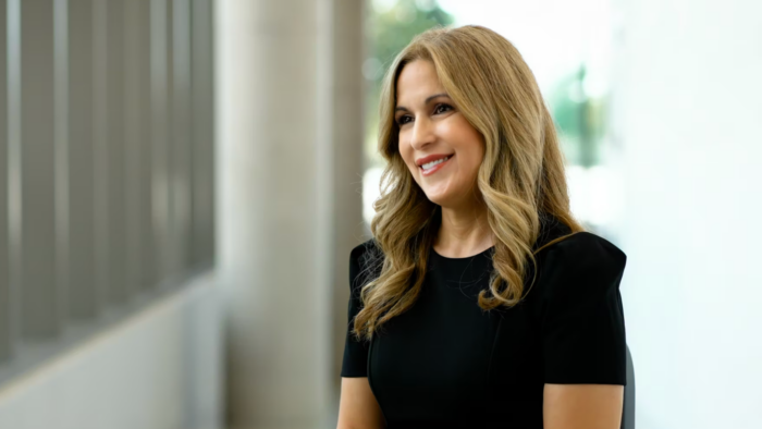 A smiling Theresa Williams sits for an interview wearing a black dress against a light, blurred background.