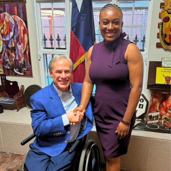 Two people posing for a photo while shaking hands. the person on the left is seated in a wheelchair while the person on the right is standing.