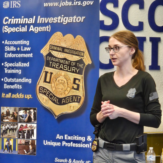 A person speaking in front of a backdrop listing information on the IRS Criminal Investigation unit.