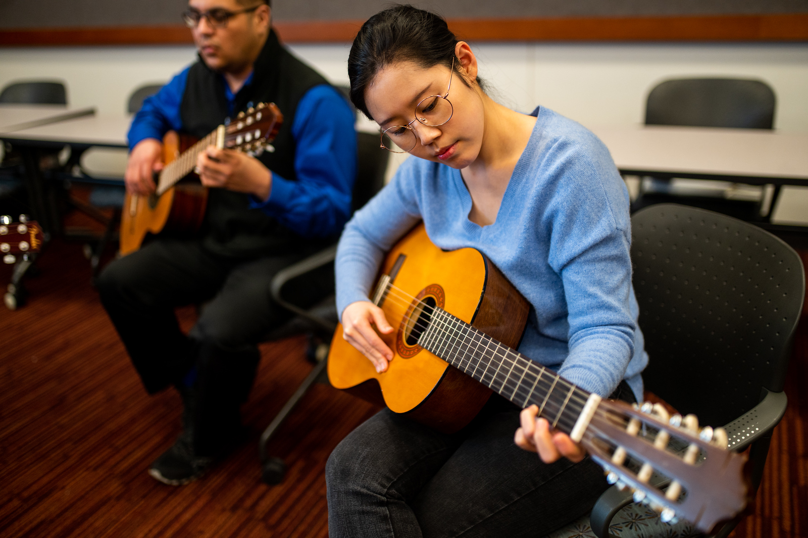 A female and male students, playing the guitar in a classroom setting.