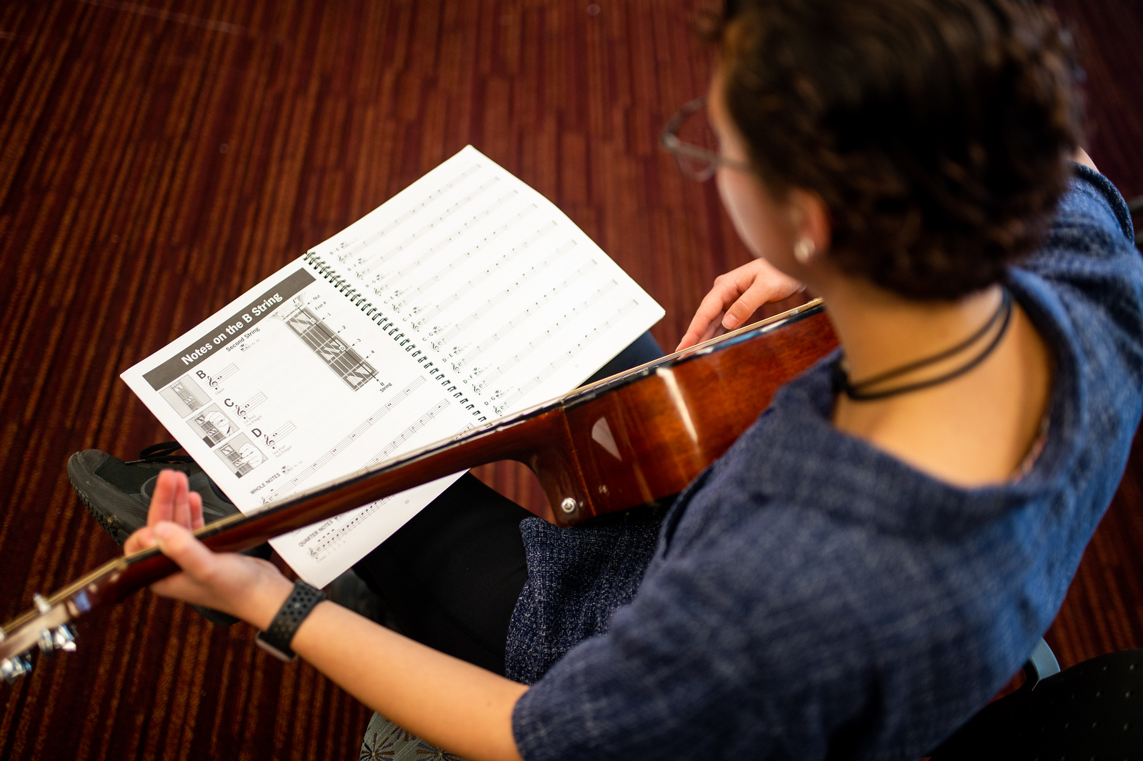 An individual playing the guitar while using a music sheet.