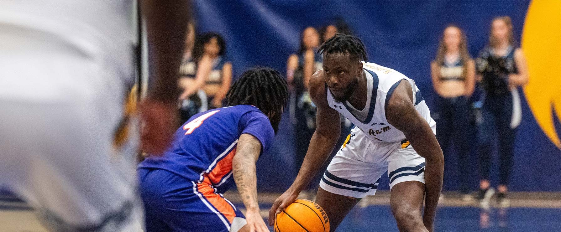 Player in white uniform on the right dribbles the ball. Player in blue uniform on the left defends the ball.