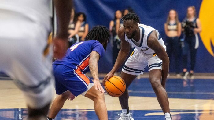 Player in white uniform on the right dribbles the ball. Player in blue uniform on the left defends the ball.