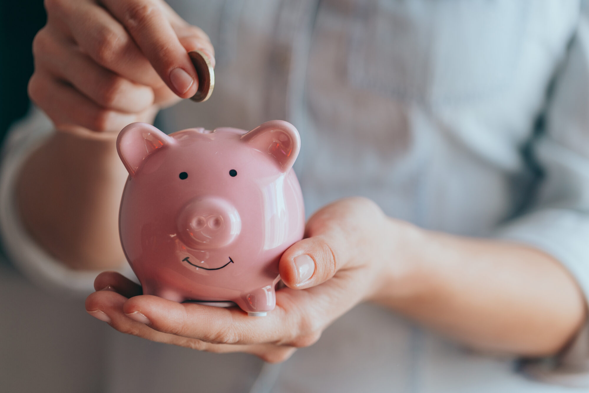 female hands puts a coin in a pink piggy bank. The concept of saving money or savings, investment