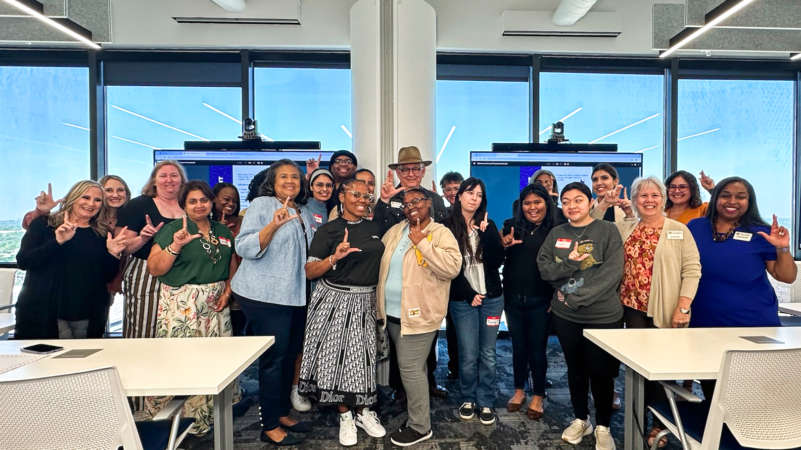 Attendees at the Culturally Relevant Literacy Seminar pose for a group photo while holding up the Lucky Lion hand gesture involving the right-hand thumb and first two fingers.