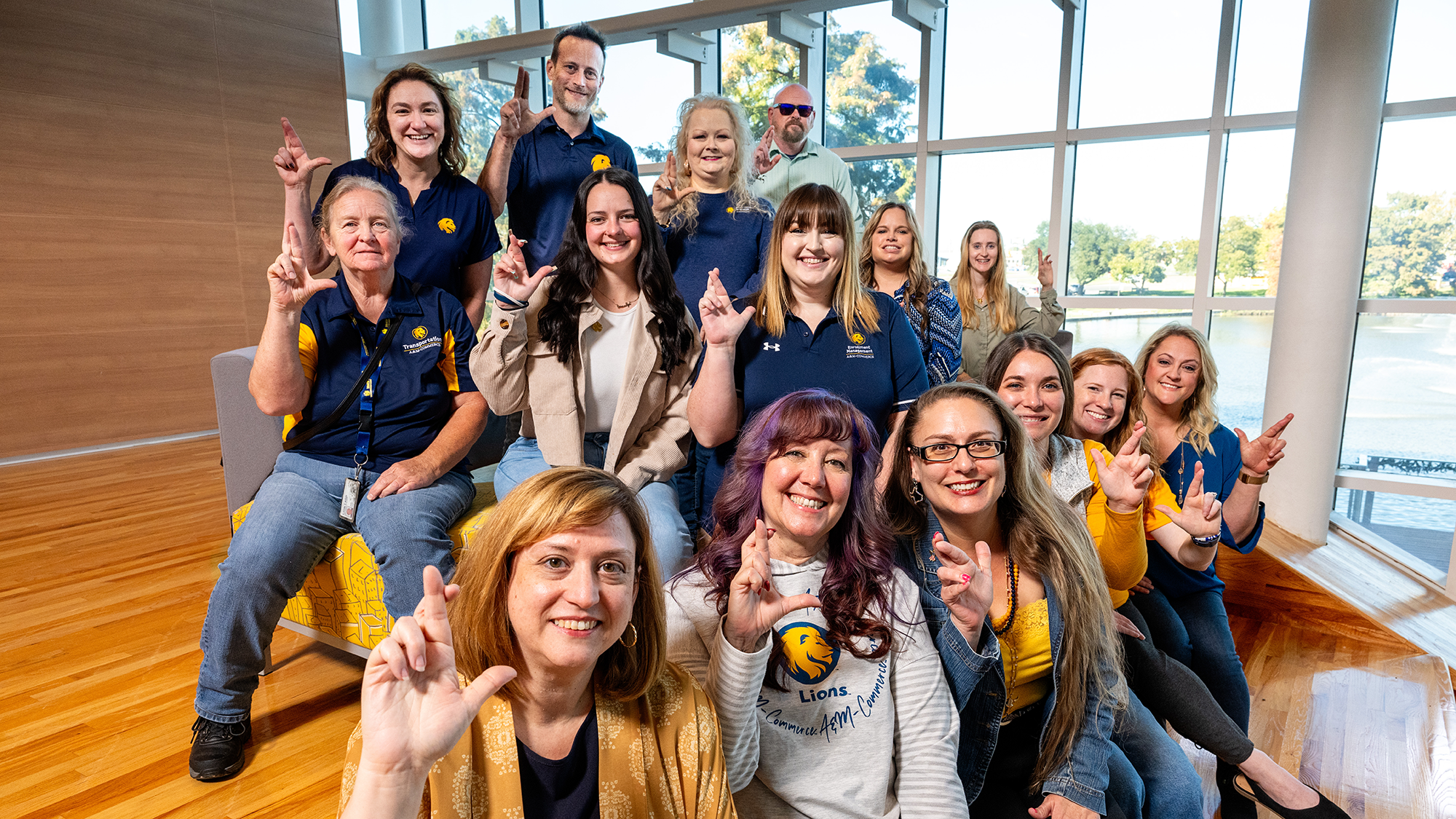 The 2025 Staff Council at East Texas A&M huddles for a group photo. Members are dressed in the school colors of blue and gold, and they're holding up the Lucky lion hand gesture.