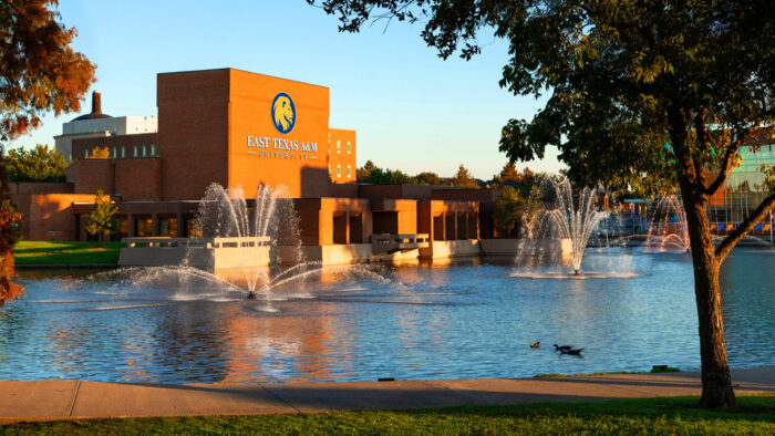 Lake in foreground and brick university building in background with university's lion head logo and the name of the university on the building.