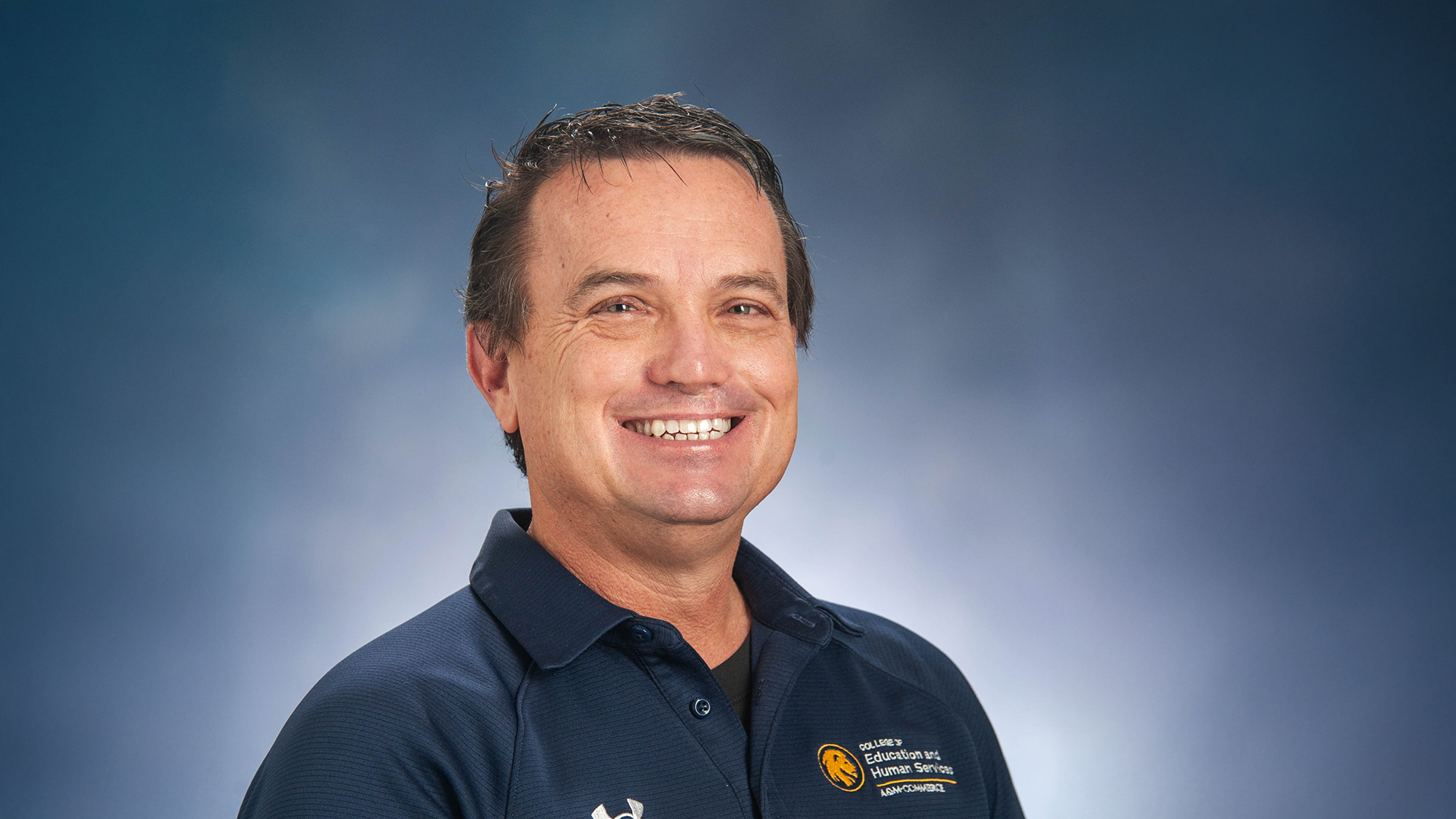 Professional photo of Brian Brumley wearing a dark blue polo shirt against a mottled blue background.