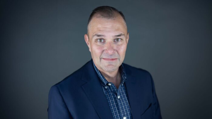 Dr. Rank wears a plaid button-up shirt and dark suit jacket for his headshot photo.