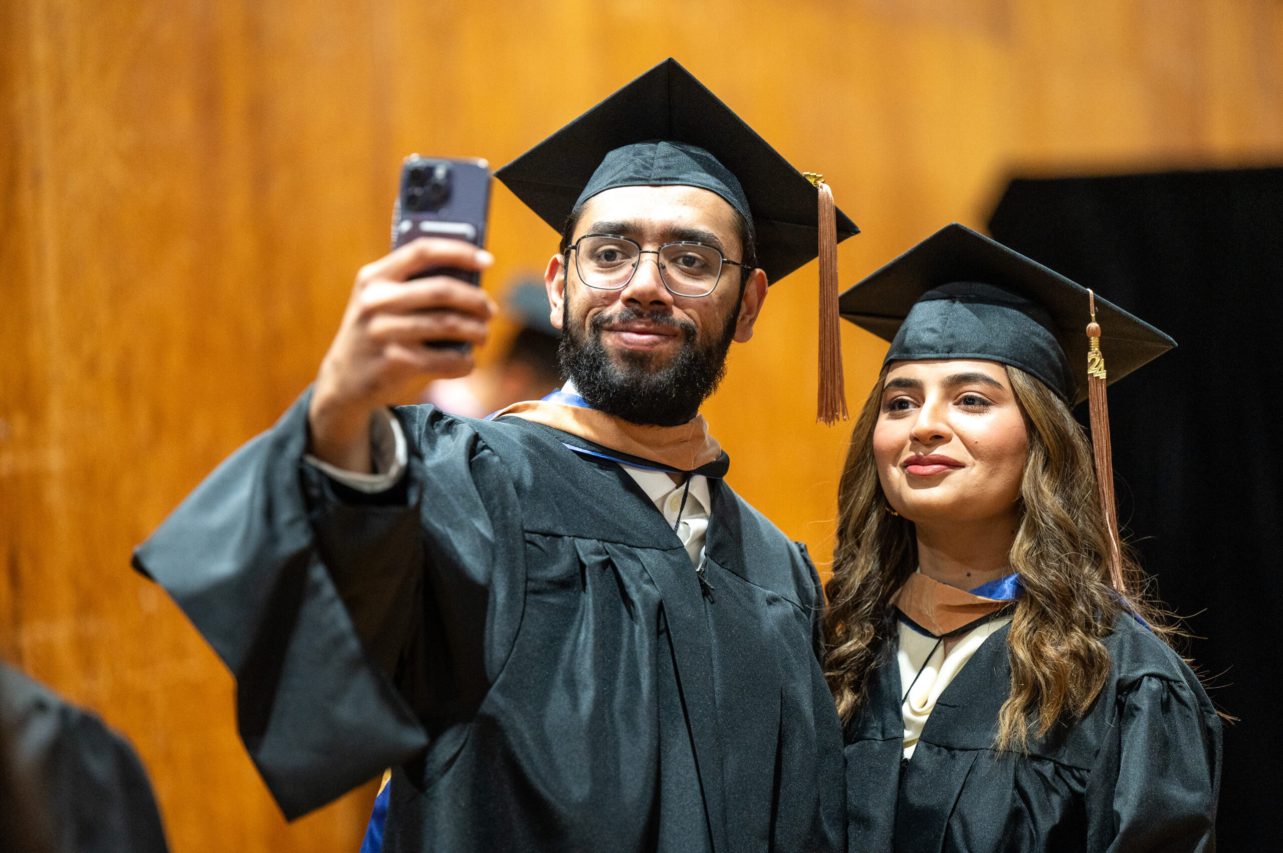 A pair of college graduates take a selfie in their caps and gowns.