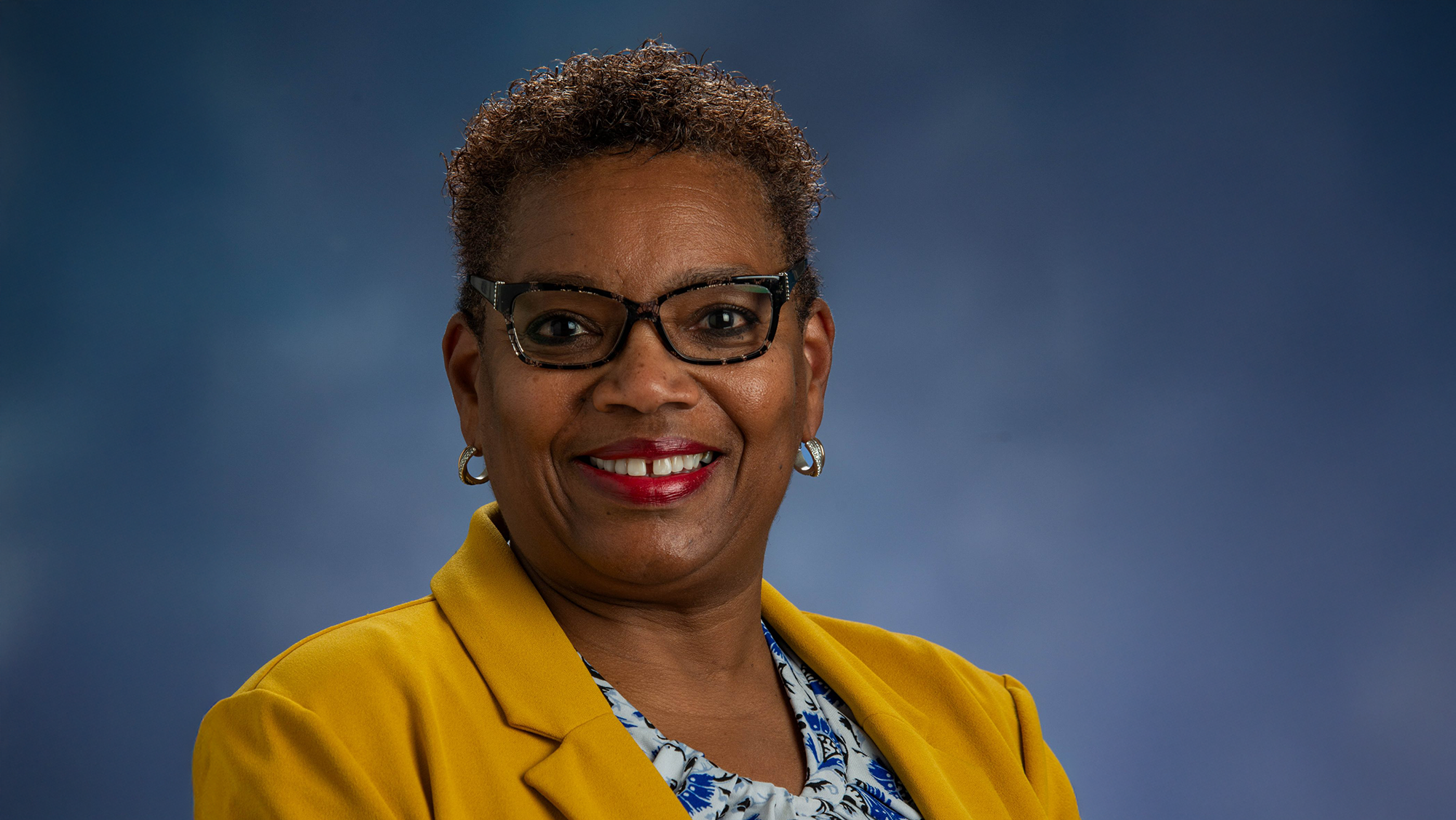 Professional photo of Dr. Sharon Ross wearing a gold blazer against a mottled blue background.