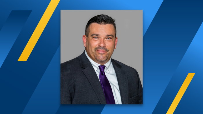 A professional headshot of James J. Branam wearing a dark suit and purple tie. The headshot is floating over a blue and gold diagonal striped background.