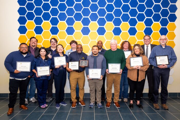 A large group of people stand posing with award plaques