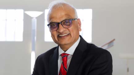 Professor smiles for camera. He is wearing a suit with white dress shirt and red tie.