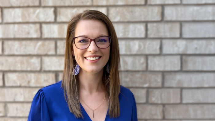 East Texas A&M alum Tina Clark wearing a blue top, standing against a light brick background.