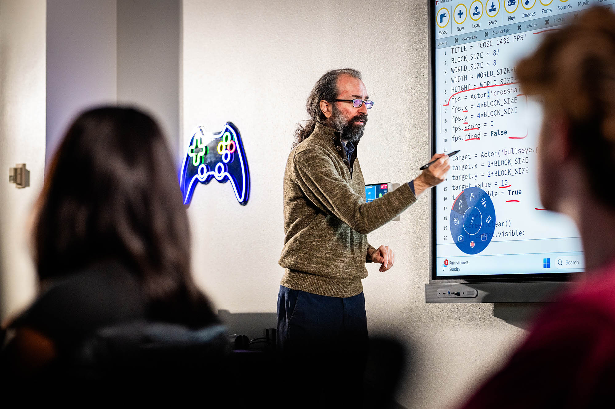 Computer science professor teaching programming concepts on a smartboard during a class at a university.