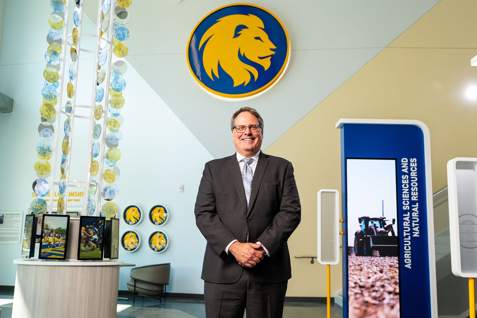 Dr. Mark Rudin, President of East Texas A&M University, standing in the Agricultural Sciences and Natural Resources building with the university logo in the background.