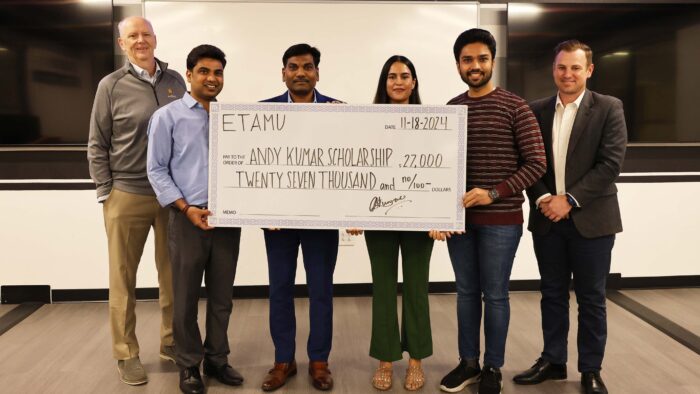 Six people smile at the camera. Four of the poeple hold an oversized check to show a gift amount.