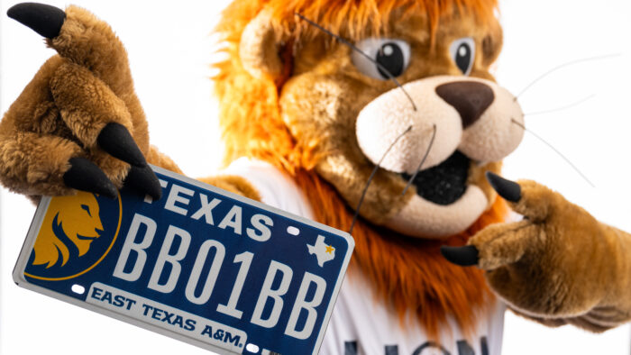 A person in a lion mascot costume holding a license plate.